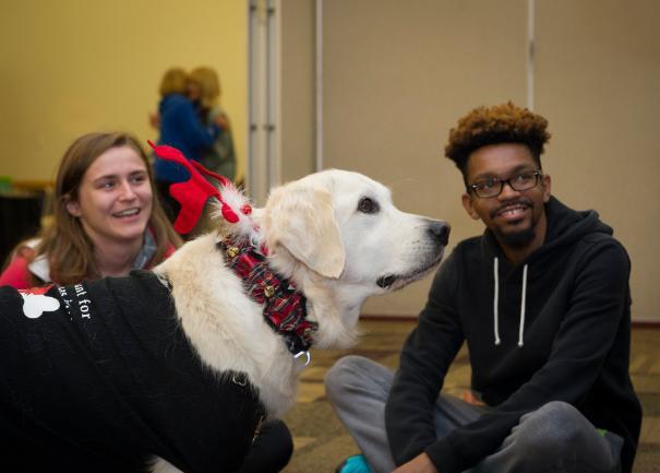 Dogs On Call therapy dog Wrigley, a golden retriever, wears a reindeer collar and is making two V C U students smile