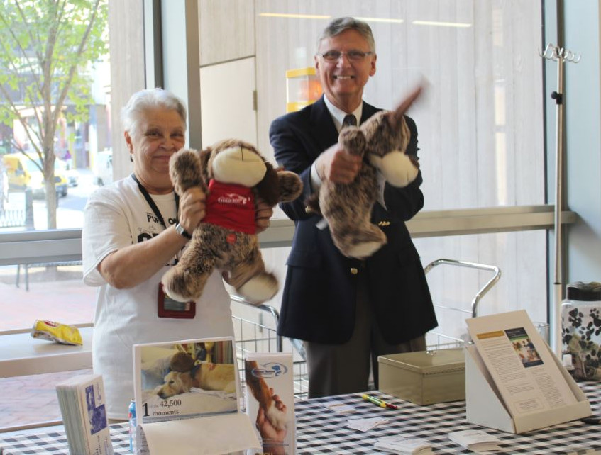 Two supporters of Dogs On Call hold PetSmart stuffed animals at aPups on the Plaza table