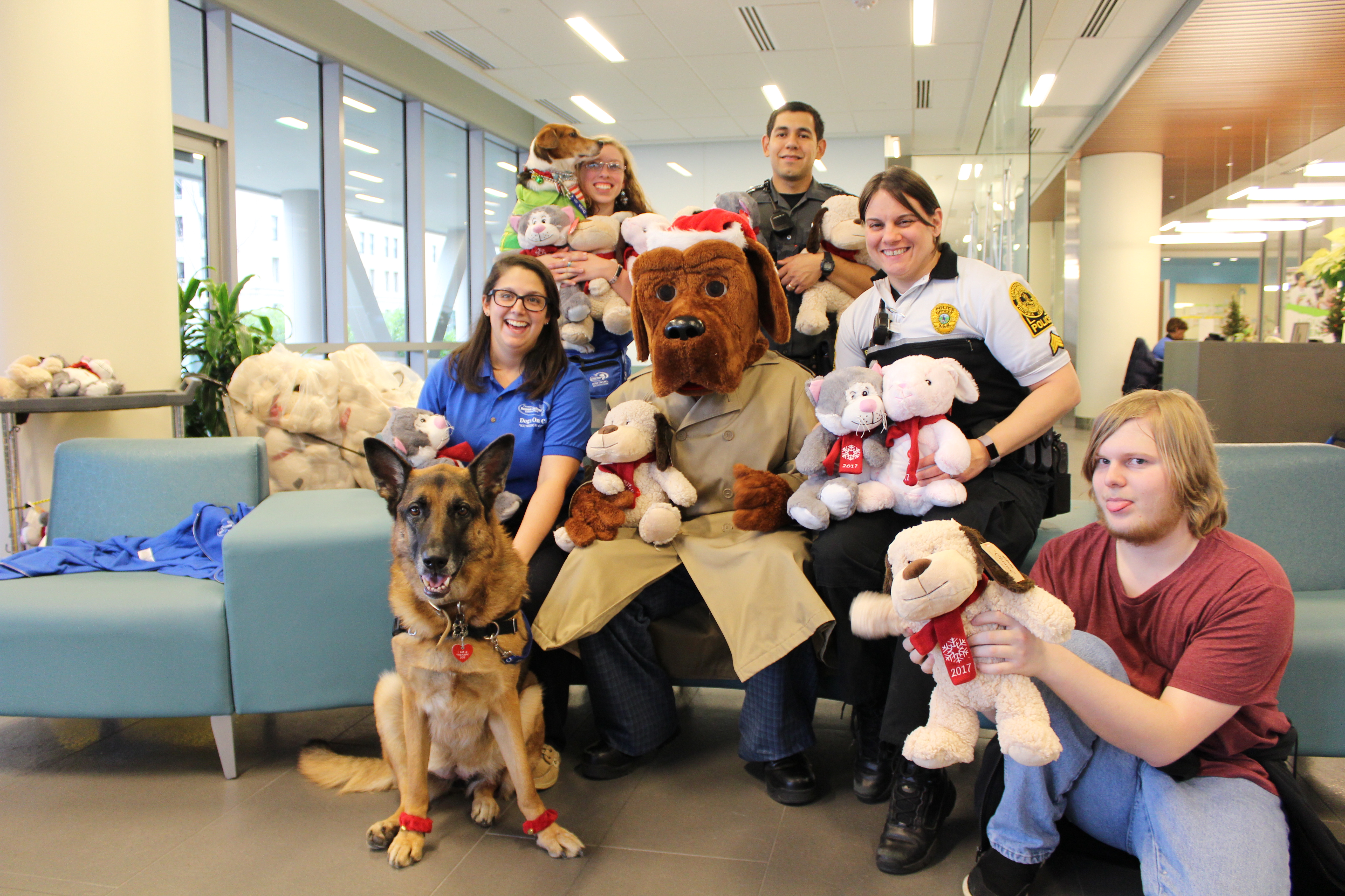 Therapy dogs Dahlia, a german shepherd, and Blake, a beagle mix, pose alongside McGruff - the costumed hound dog mascot for the V C U police - two police officers, their handlers and another friend who are all holding stuffed animals.
