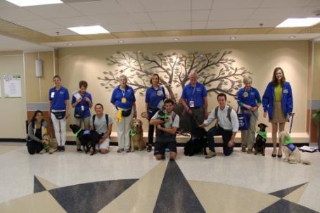 Several Dogs On Call therapy dogs pose with their handlers behind them and a few V C U students pose alongside the dogs.