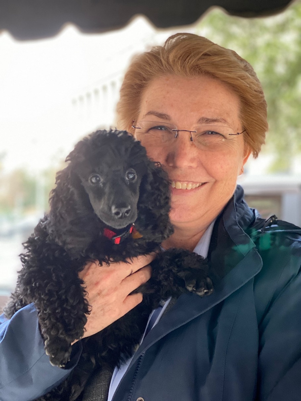 Dr. Gee smiles as she is holding a black miniature poodle puppy.  The puppy is extremely cute.