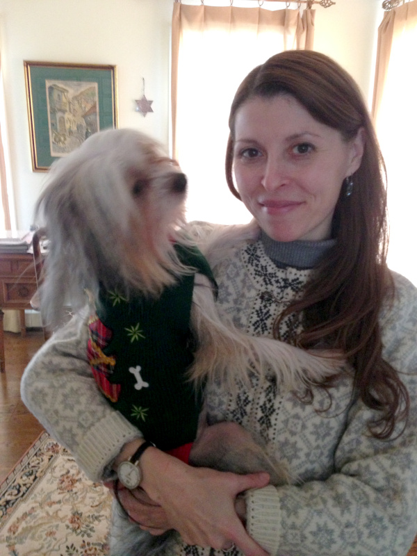 A woman in a white Christmas sweater is cradling a Chinese Crested dog in a green christmas sweater