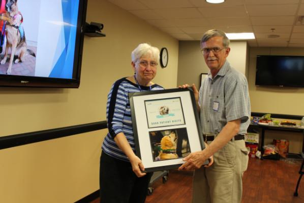 Team Daisy holds a framed photo of Daisy, a yellow lab, and a recognition certificate acknowledging Daisy's 5,000 patient visits